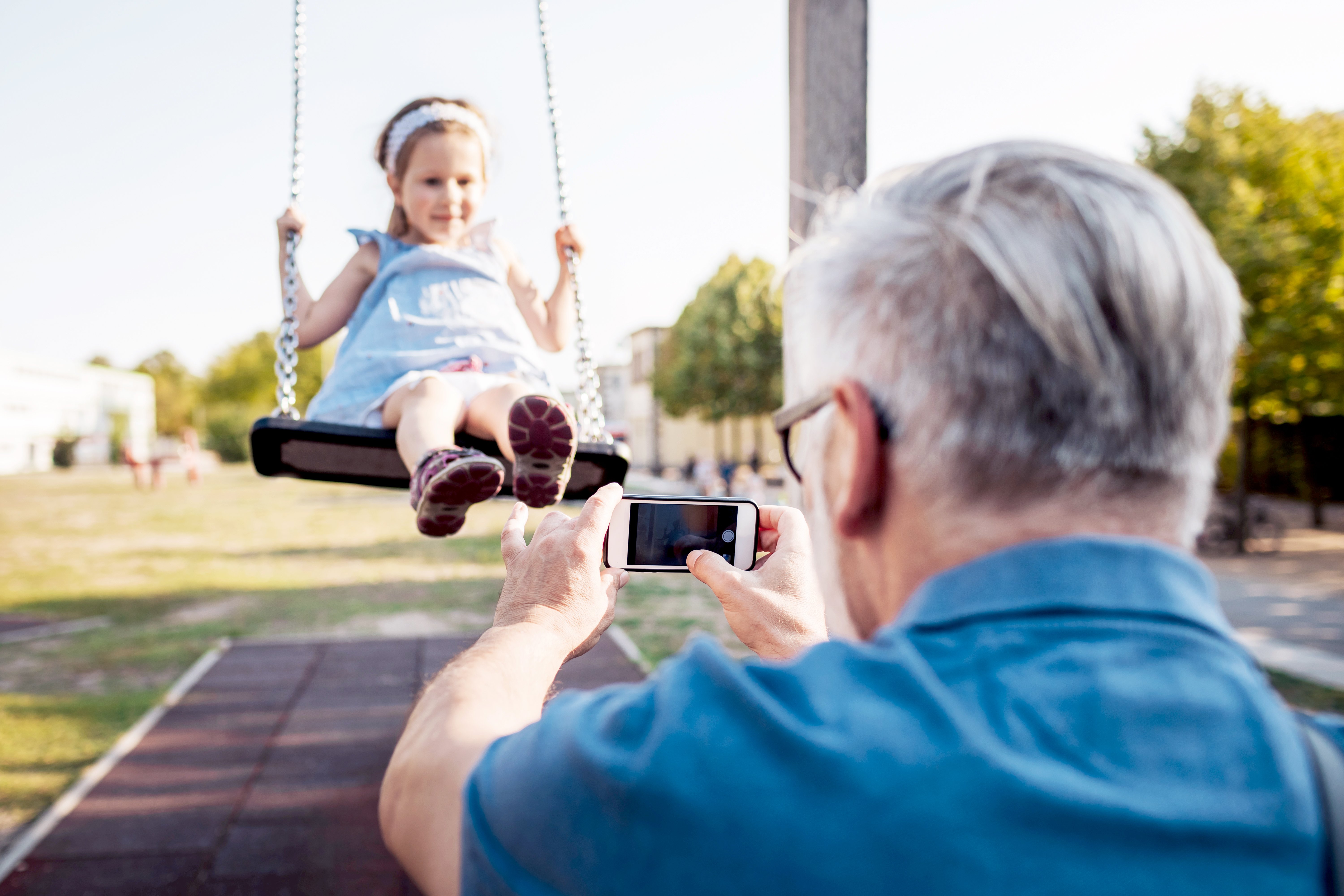 Older man taking a video of his granddaughter on a swing
